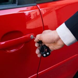A person holding the door handle of a red car.